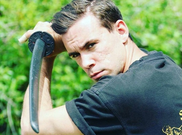 Man with a serious face poses with a plastic sword. 